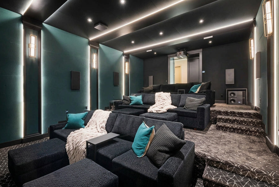A luxury home theater interior with tiered seating, dark textured sofas, teal accent pillows, and integrated LED lighting on dark teal and black walls.