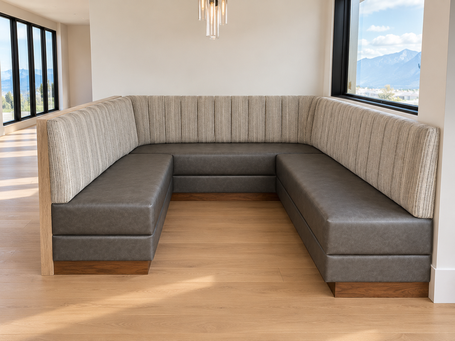An L-shaped upholstered booth seating unit with ribbed beige fabric upholstered backrests and dark gray seat cushions, installed in a modern room with light wood floors and large windows showing a mountain view.