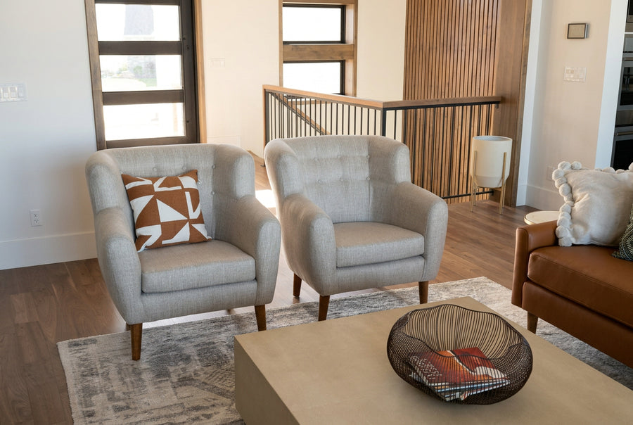Two light beige upholstered armchairs with dark wood legs placed on a patterned rug in a modern living room setting.